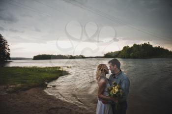 Newly-married couple embraces against lake.