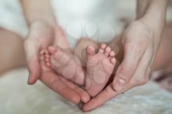 Feet of the baby in hands of mother.
