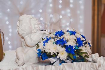 The figure of an angel near the bouquet of white and blue flowers.