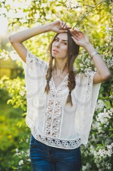 Girl in white blouse stands in the background of a blossoming Apple tree.