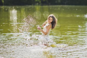 Girl squirts water standing waist-deep in the lake.