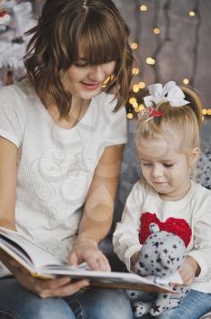 Mother and daughter looking in a beautiful book sitting around the Christmas decorated fir.