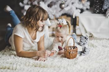 Mother and daughter lying on the carpet under white decorated Christmas tree.