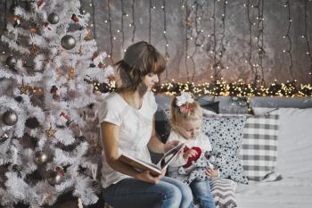Mother year-old daughter read the book in Christmas decorations.