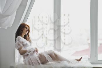 Beautiful girl in a white robe sitting on the windowsill.