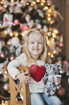 Girl with big red heart on the clothes near the Christmas tree.