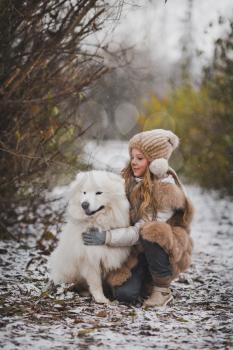 The girl petting the dog on the walk in the late autumn.