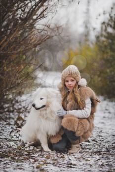 The girl petting the dog on the walk in the late autumn.