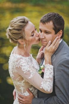 The bride in a translucent dress kissing her husband on the cheek.