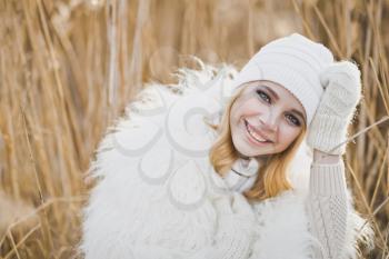 Close-up portrait of girl in white furry jacket and hat in the winter among the reeds.