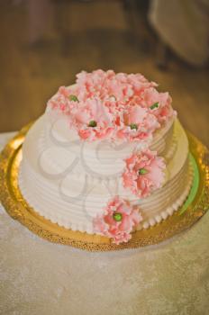 A big cake made of beige cream decorated with pink flowers.