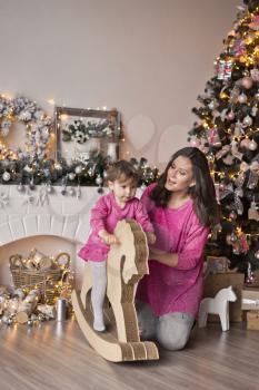 Girl in pink dress is riding on horse-rocking around the Christmas tree.