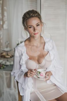 Girl with beautiful shapes in a transparent dressing gown drinking tea.