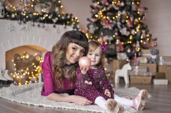 Portrait of mother with her daughter play near the fireplace and Christmas tree.