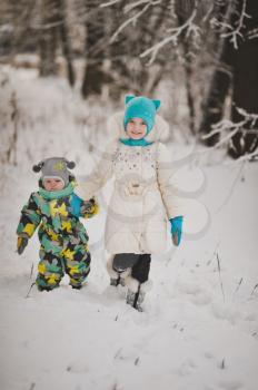 Two small children walk in the snowy woods.