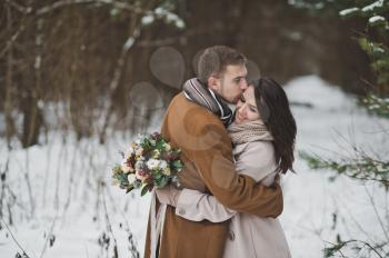 Newlyweds hug each other against the background of winter forest.