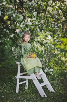 The girl in the green dress and apron on the background of the garden.