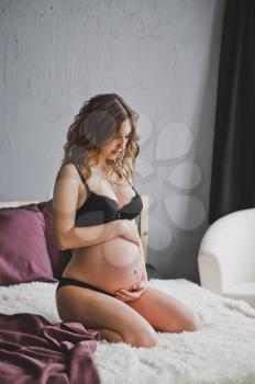 Happy pregnant girl in black underwear stroking big belly with baby.