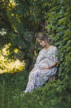 Portrait of a pregnant girl walking in the summer garden.