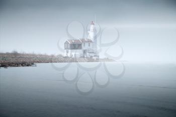 lighthouse in the fog is on the pier into the sea. mystical landscape. twilight