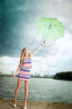 happy girl under an umbrella walks in the rain during the summer along the river against the background of the city