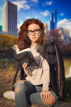 red-haired girl is sitting with a book in the central park in Manhattan in New York