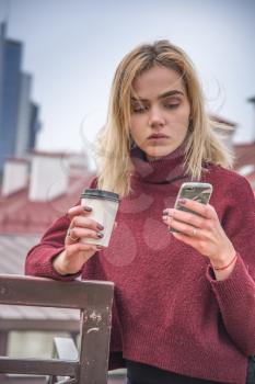a girl drinks coffee and looks into the phone