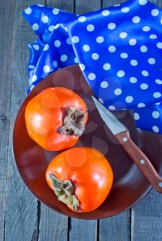 Ripe persimmons on plate and on table