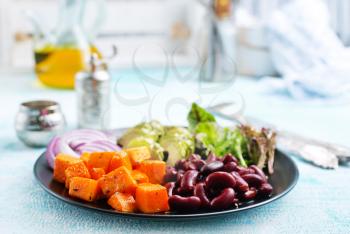 ingredients for salad, baked pumpkin, avocado and red beans on black plate