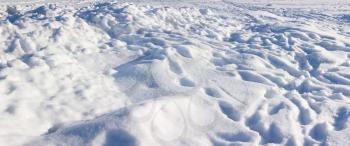 Rough snow surface with snowdrifts, traces and footprints under bright sunlight