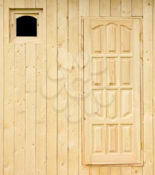Wooden rural house wall under construction made of the rough raw boards with the unfinished door and a small square window