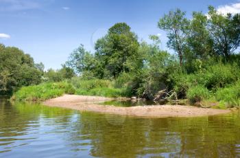 Beach of calm river with green trees under blue sky, summer rural landscape