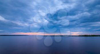Blue tranquil minimalist landscape with smooth surface of the lake with calm water with horizon under cloudy dramatic sky, beautiful blue calm natural background.