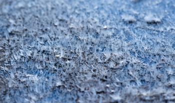 White hoarfrost crystals on flat surface closeup macro view with selective focus, shallow depth of field, blue background.