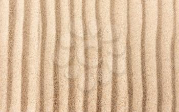 Yellow dry sand surface with grooves and wavy lines close-up top view with shallow depth of field nature background