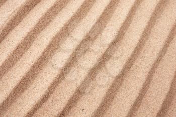 Dry sand surface with grooves and wavy lines close-up diagonal top view with shallow depth of field nature background