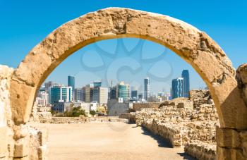 Ancient arch at Bahrain Fort with Manama skyline. A UNESCO World Heritage Site in the Middle East