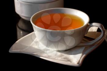 Cup of black tea on a saucer with a napkin and sugar bowl on a dark background