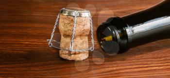 Empty champagne bottle and muzzle and cork closeup on wooden surface