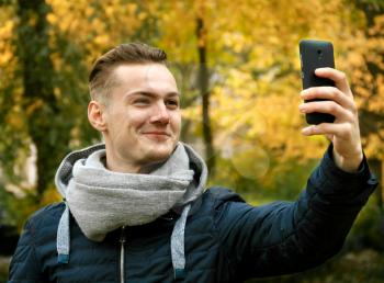 Cute young man with smartphone in autumn park