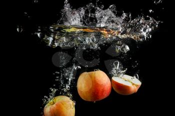 Apples falling into the water with a splash and air bubbles. Fresh apples in water on black background. Healthy food. Wash fruits.