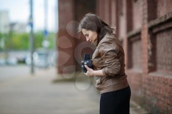 Female photographer taking photos in the street.  Woman with an old vintage camera outdoor. Shallow depth of field. Selective focus on model.