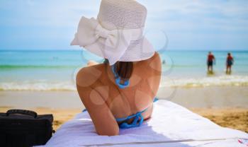 Back view of a woman in bikini and white hat with bow on tropical beach. Shallow depth of field. Selective focus.