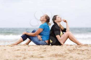 Two girls sitting outdoors. Two pretty young women sitting and relaxing on the sand on the beach. Selective focus on models.