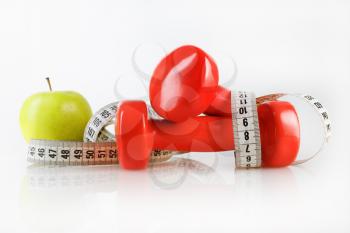 Apple, measuring tape and dumbbells. Fitness concept. Composition on the theme of healthy lifestyles.