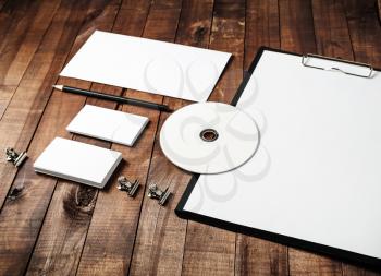 Photo of blank stationery set: paper, clipboard, letterhead, business card, envelope, cd and pencil on vintage wooden table background. Corporate identity template for branding identity for designers.