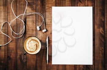 Blank branding template on vintage wooden table background. Blank white letterhead, pen, headphones and coffee cup. Top view.