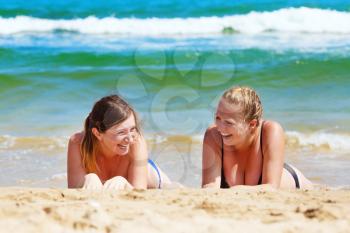 Happy laughing girls lying on the sand on a background of turquoise sea water. Two cheerful young woman sunbathing on the beach. Selective focus.