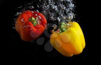Fresh paprika splash in water with air bubbles. Red and yellow paprika in water on black background. Healthy food. Wash vegetables.