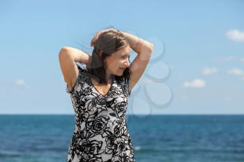 Young long-haired woman posing on a background of blue sky and sea on a clear sunny day. Blurred background. Focus on model.